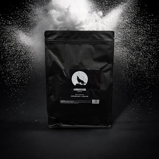 Eine schwarze Tüte Crunchy Chalk von MoonKing mit einem Wolfslogo auf dunklem Hintergrund. Ein dynamischer Schwall weißen Magnesiastaubs umgibt die Verpackung und verkörpert die abenteuerliche Essenz, die Kletterfans so schätzen, und unterstreicht den Ruf des Produkts für außergewöhnlichen Grip.